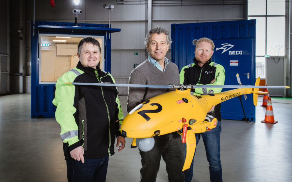 Foto van drie mannen die een gele drone vasthouden